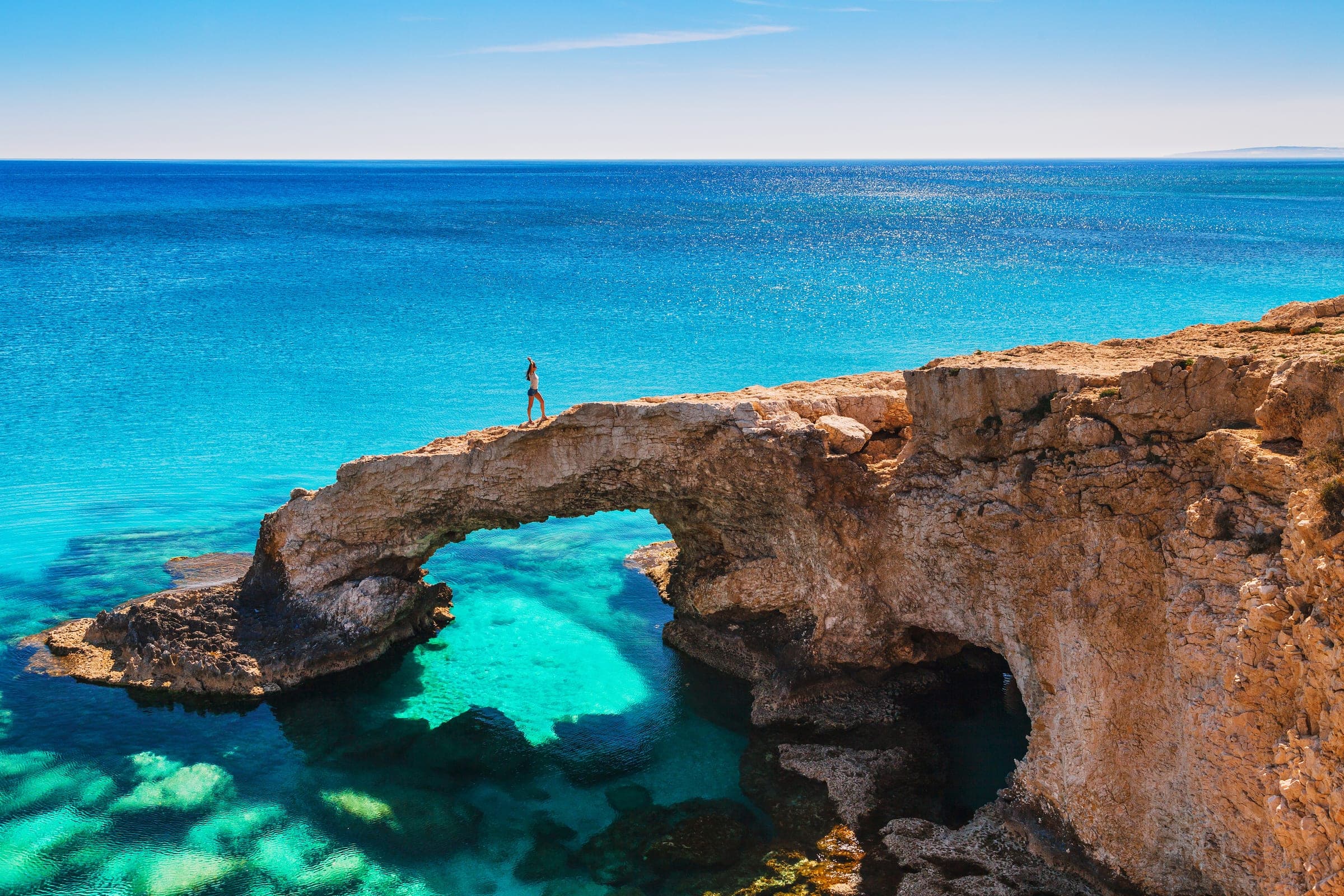 Wandelaar op de natuurlijke rotsboog boven de turquoise zee bij Kavo Greco, Cyprus