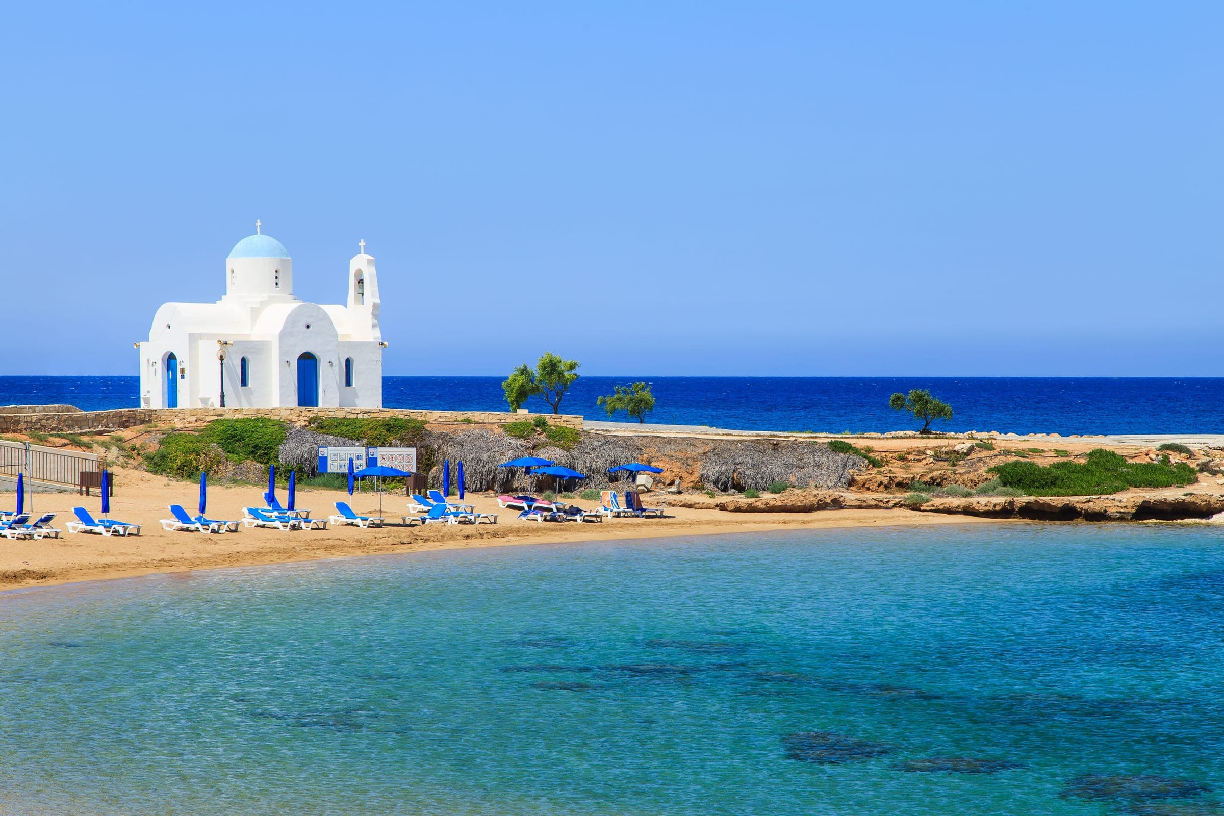 Wit kerkje met blauwe koepel aan een rustige zandbaai in Protaras, Cyprus