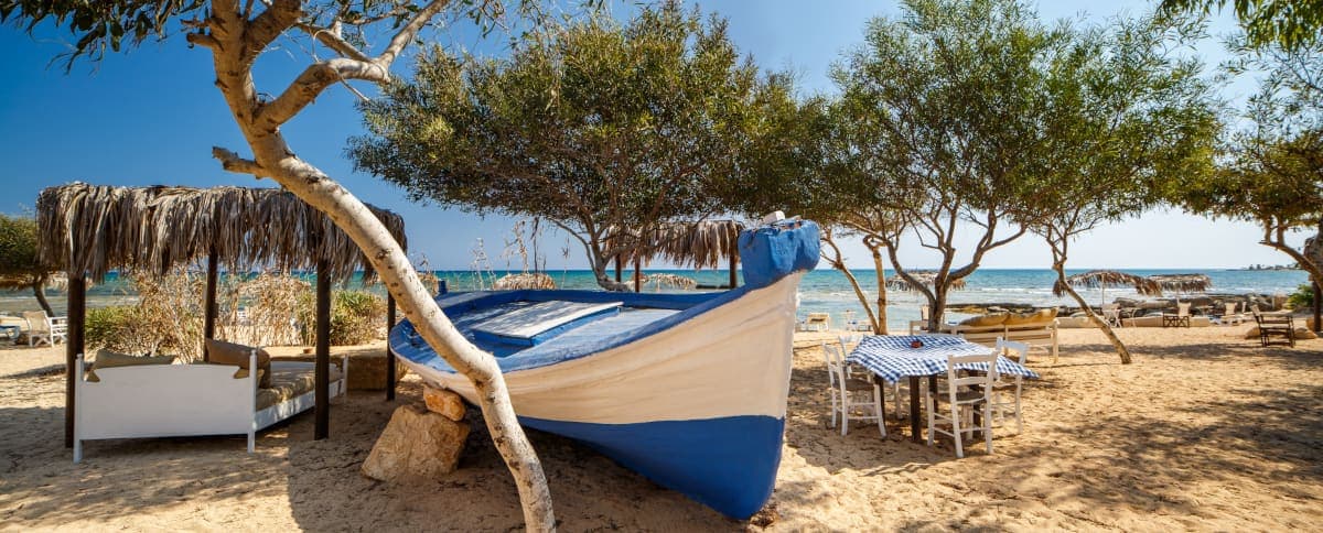 Strandtaverna op Cyprus met traditionele houten vissersboot en tafels aan zee